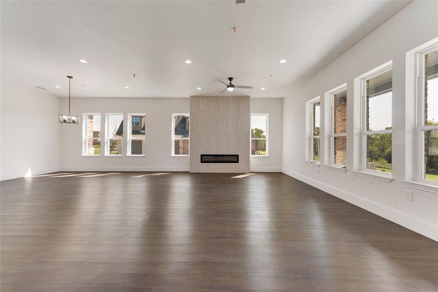 Spacious room featuring wood-finish flooring, a linear fireplace with a textured surround, recessed lighting, and multiple windows Spacious room featuring wood-finish flooring, a linear fireplace with a textured surround, recessed lighting, and multiple windows