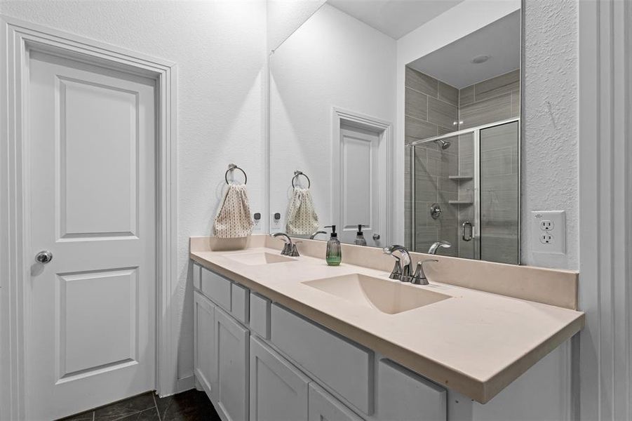 Bathroom featuring double vanity, a stall shower, and a textured wall