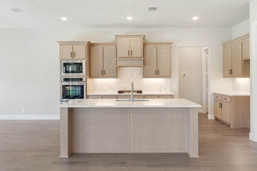 Kitchen with large center island, light wood cabinets, white countertops, and stainless steel double oven