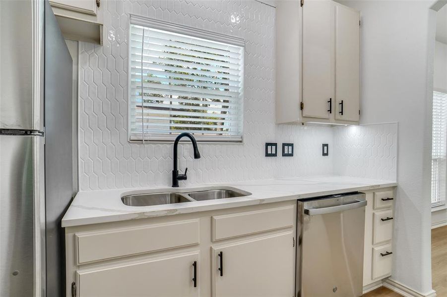 Kitchen with light stone counters, sink, white cabinets, and appliances with stainless steel finishes