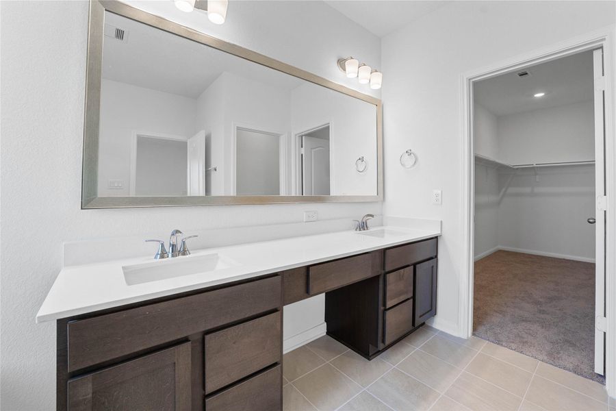 This beautifully updated primary bathroom is move-in ready! It showcases stained cabinetry paired with light countertops, dual vanity sinks, a large framed mirror, a spacious walk-in closet with built-in shelving, high ceilings, custom paint, and stylish modern finishes throughout.