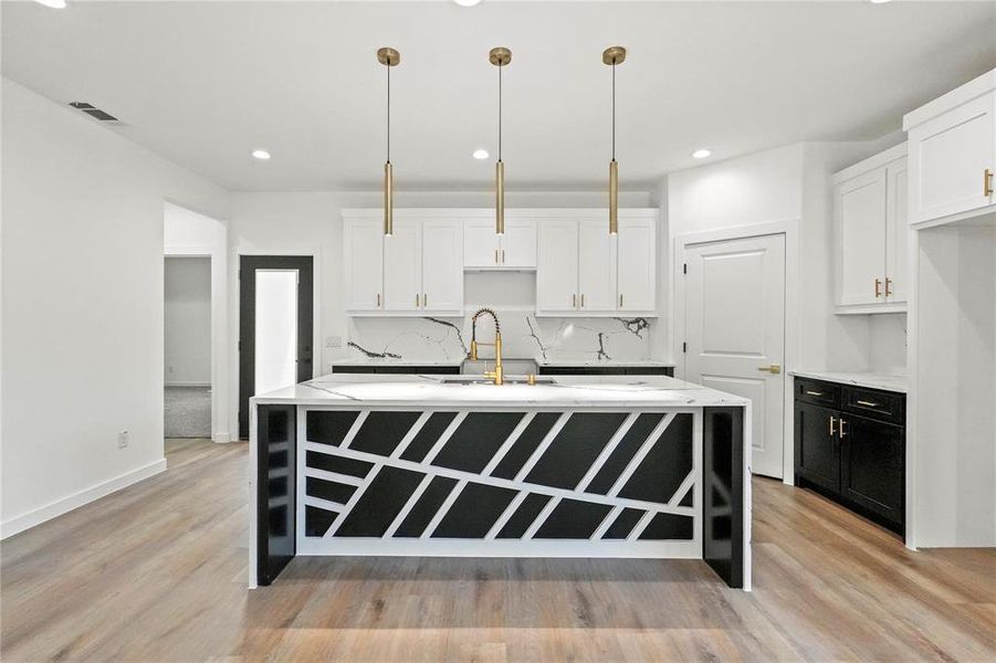 Kitchen with white cabinets, light wood-type flooring, hanging light fixtures, and an island with sink