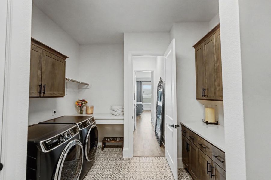 A well-appointed laundry room features dark wood shaker cabinetry that provides ample storage, complemented by quartz countertops and an geometric pattern floor tile. The space includes a hanging rod and a folding counter.