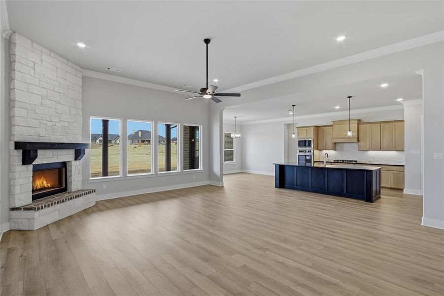 Unfurnished living room with a ceiling fan, ornamental molding, a stone fireplace, light wood-type flooring, and recessed lighting