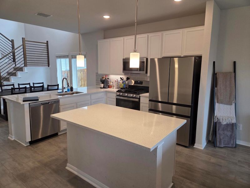 Open-concept kitchen featuring an island with a light-toned countertop, white cabinetry, stainless steel appliances, and wood-finish flooring