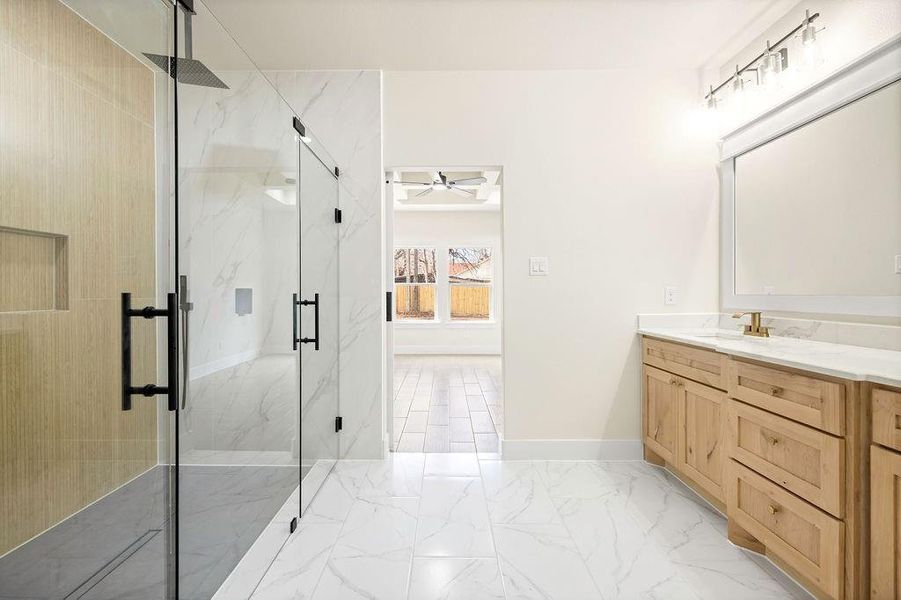 Bathroom with marble finish floor, a marble finish shower, baseboards, and vanity