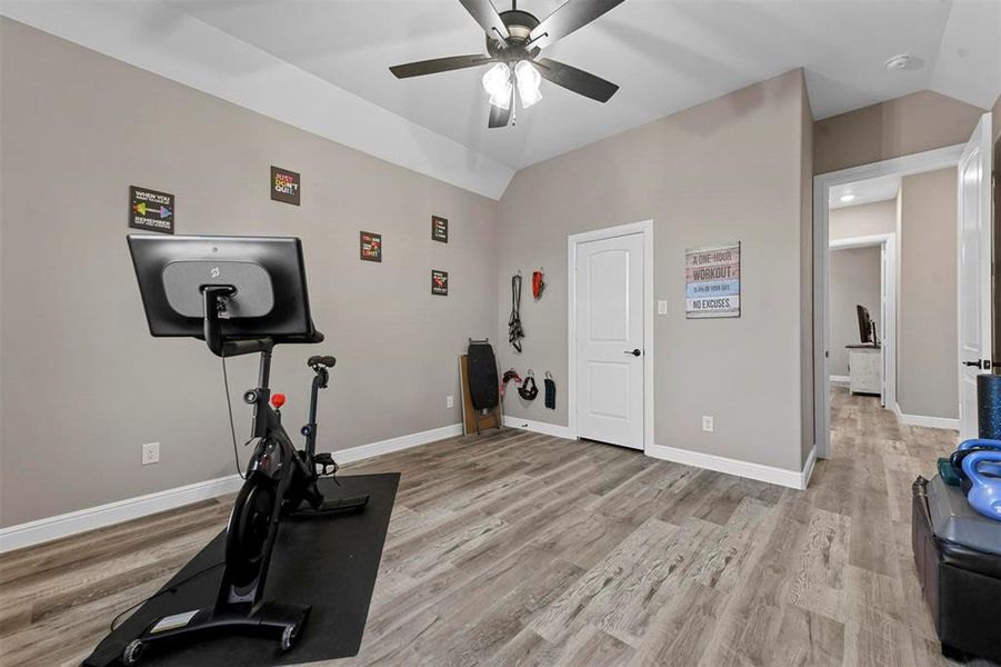 Exercise area featuring ceiling fan, lofted ceiling, and light wood-type flooring