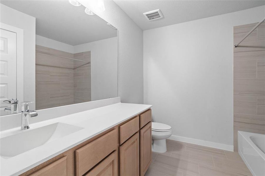 Secondary bath features tile flooring, bath/shower combo with tile surround, white stained wood cabinets, beautiful light countertops, mirror, dark, sleek fixtures and modern finishes.