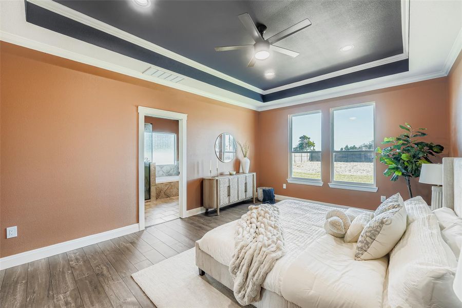Bedroom featuring crown molding, wood-type flooring, a raised ceiling, ensuite bathroom, and ceiling fan