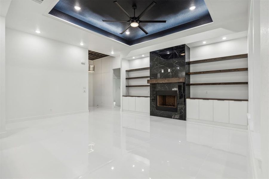 Unfurnished living room featuring a premium fireplace, ceiling fan, tile patterned flooring, and a raised ceiling