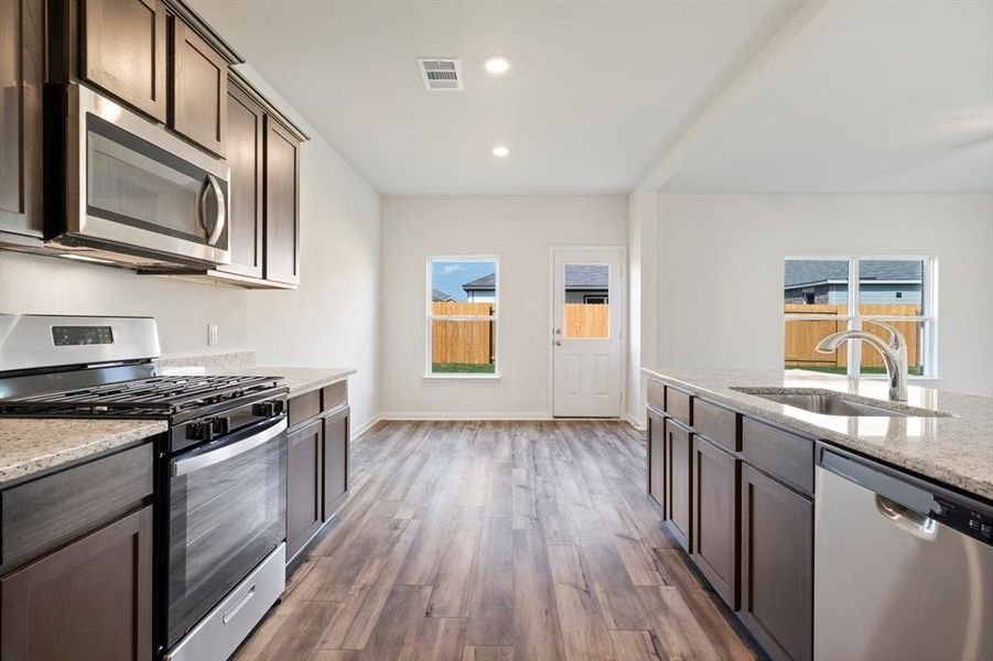 Kitchen featuring stainless steel appliances, sink, dark brown cabinets, dark hardwood / wood-style floors, and light stone countertops