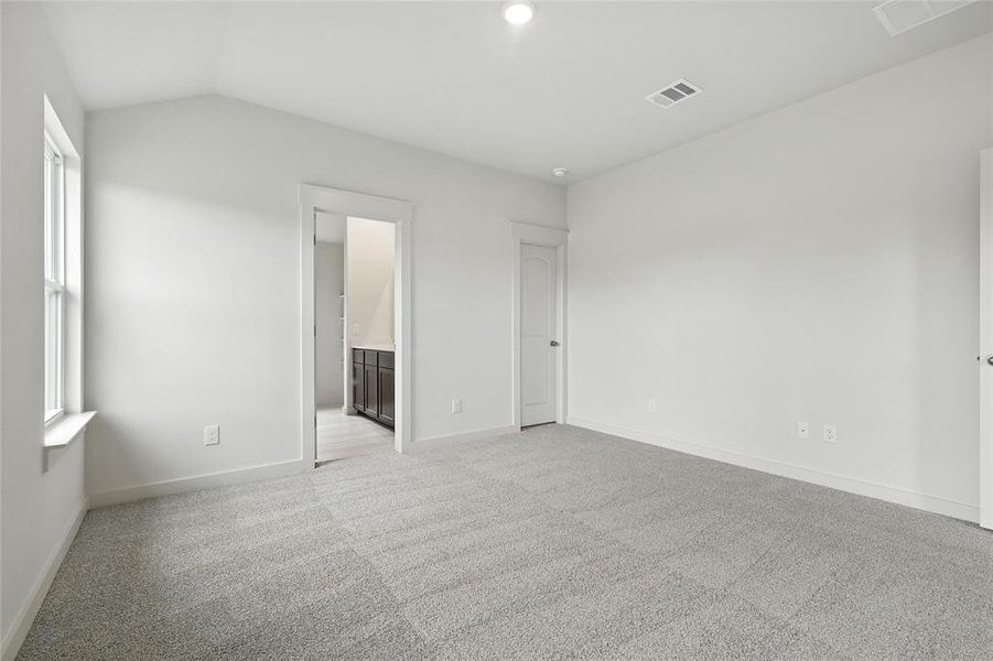 Unfurnished bedroom featuring light carpet, vaulted ceiling, multiple windows, and connected bathroom Unfurnished bedroom featuring light carpet, vaulted ceiling, multiple windows, and connected bathroom