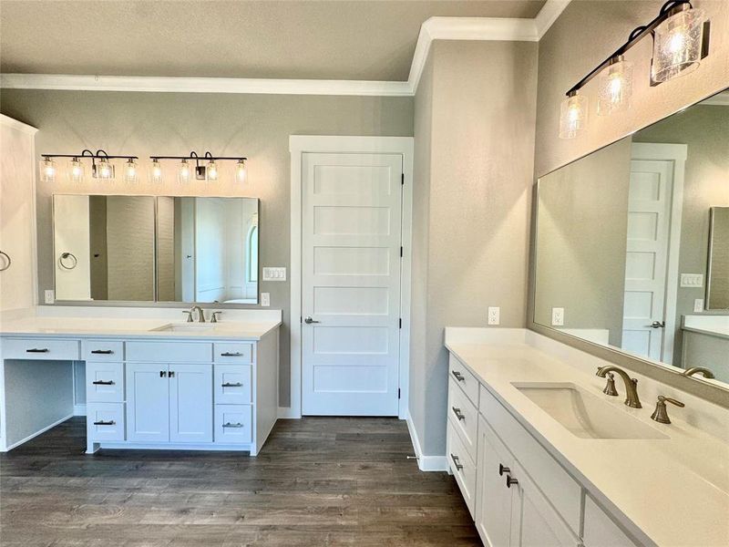 Bathroom featuring ornamental molding, wood finished floors, two vanities, and baseboards