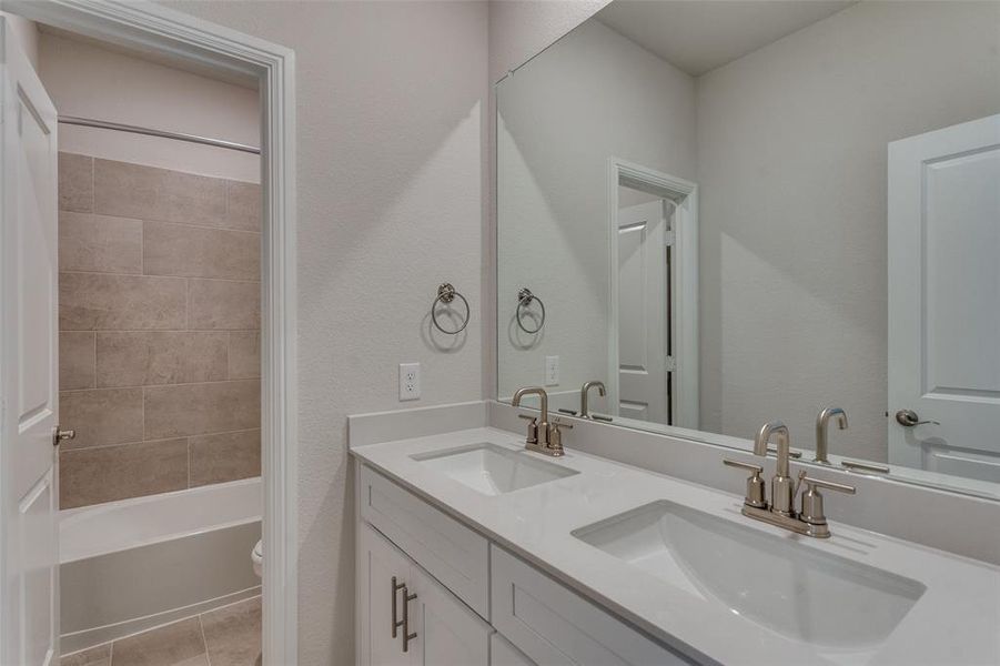 Full bathroom with double vanity, bathtub / shower combination, a textured wall, and light tile patterned flooring Full bathroom with double vanity, bathtub / shower combination, a textured wall, and light tile patterned flooring