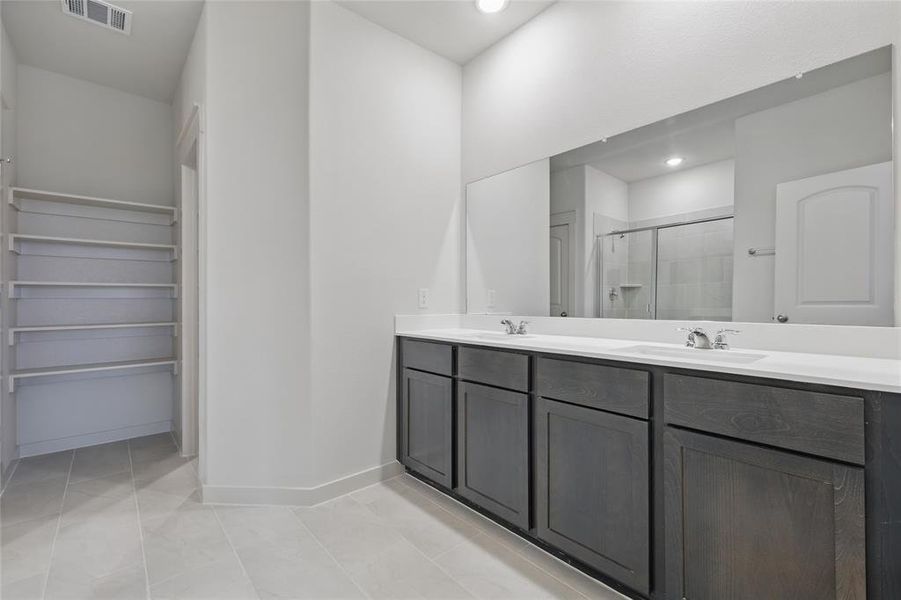 Full bathroom with double vanity, a stall shower, and a walk in closet