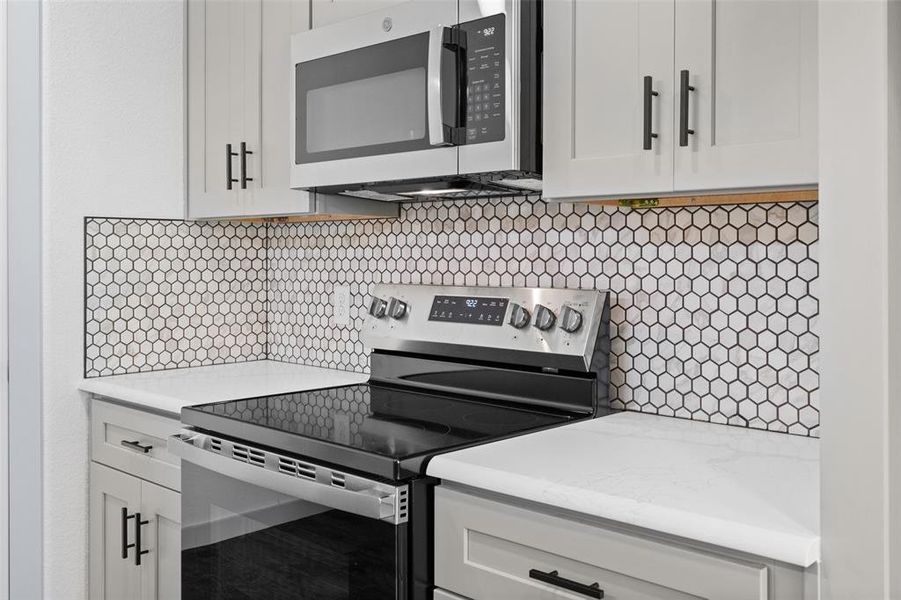 Kitchen featuring stainless steel appliances, white cabinetry, backsplash, and light stone counters