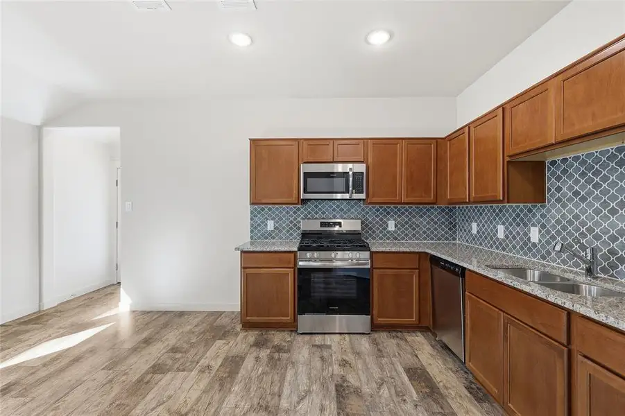 Kitchen featuring brown cabinetry, light stone countertops, appliances with stainless steel finishes, and tasteful backsplash Kitchen featuring brown cabinetry, light stone countertops, appliances with stainless steel finishes, and tasteful backsplash