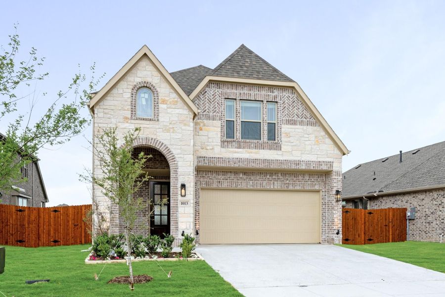 Two-story brick and stone home with arched entry, two-car garage, and manicured front lawn