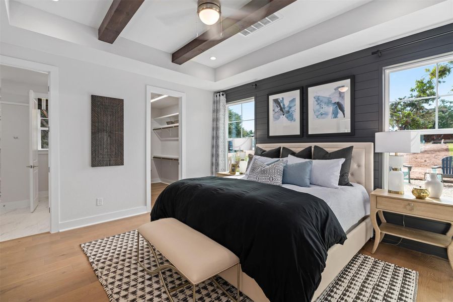Bedroom featuring beamed ceiling, a walk in closet, wood finished floors, a ceiling fan, and recessed lighting. The photos shown are of a completed home with the same floor plan and may not reflect the exact finishes, features, or layout of the home currently under construction.