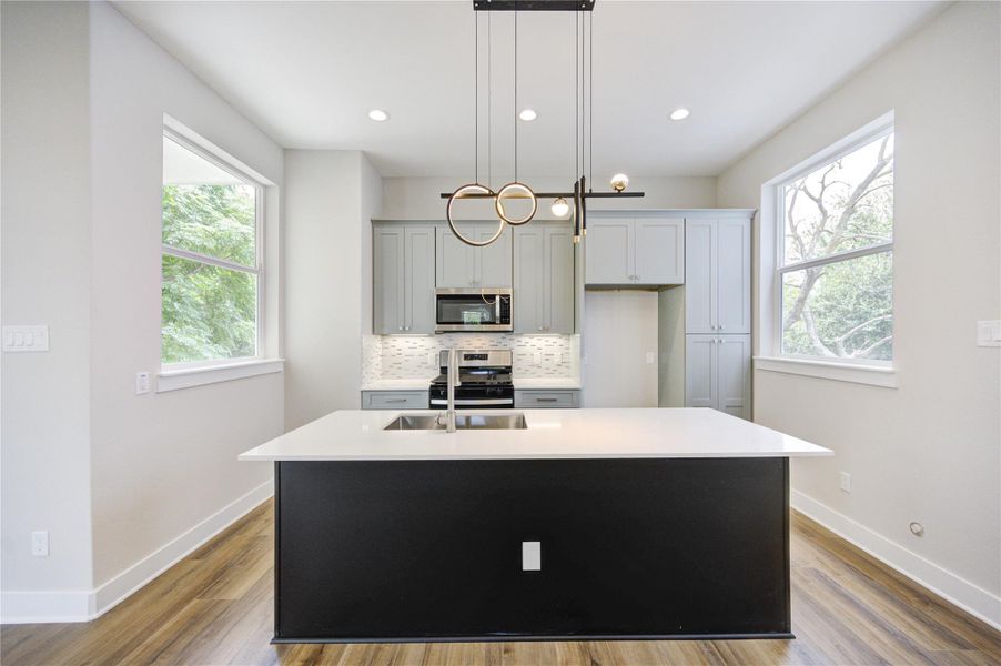 Light filled kitchen with two-tone cabinetry. quartz countertops and stainless-steel appliances. Large island with designer fixtures.