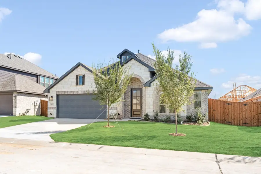 Single-story home with stone and brick exterior, arched entry, two-car garage, and green front lawn with young trees.