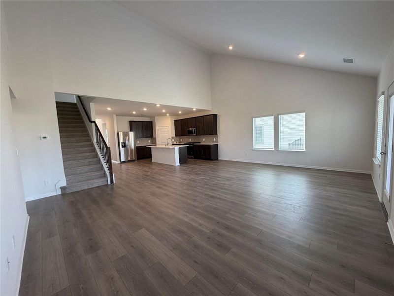 Unfurnished living room featuring high vaulted ceiling, stairway, recessed lighting, and dark wood finished floors