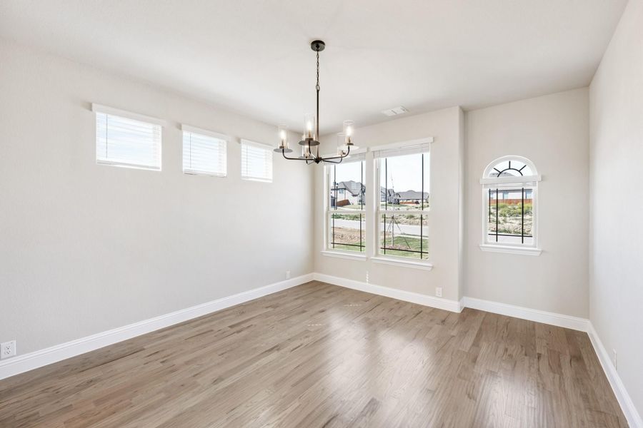Empty dining room with hardwood floors, chandelier, and large windows with arched accent window