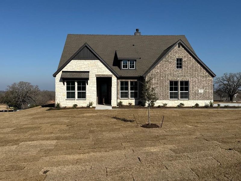 View of front of home with stone siding, a front yard, a chimney, and a shingled roof