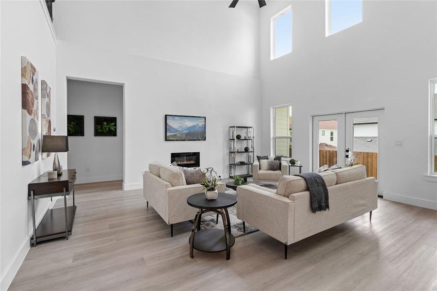Living room featuring a glass covered fireplace, light wood finished floors, a towering ceiling, french doors, and a ceiling fan Living room featuring a glass covered fireplace, light wood finished floors, a towering ceiling, french doors, and a ceiling fan