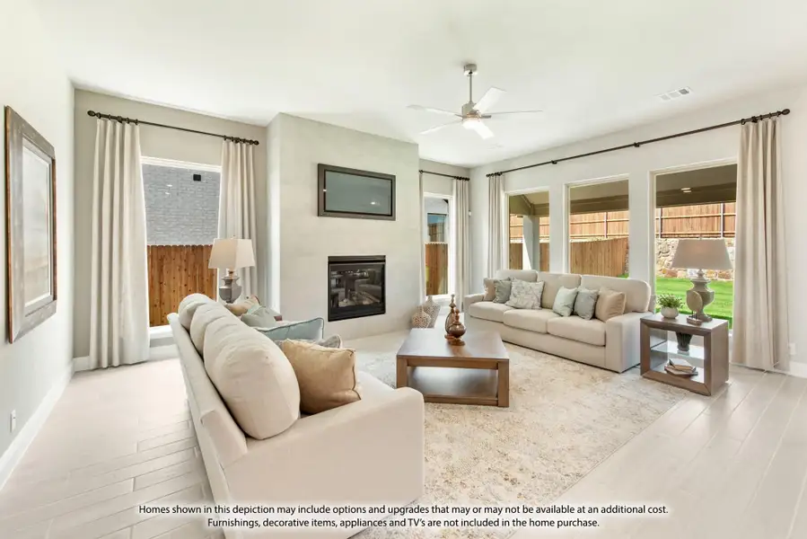 Living room with tile fireplace, ceiling fan, large windows, and neutral sofas on light wood floors Living room with tile fireplace, ceiling fan, large windows, and neutral sofas on light wood floors