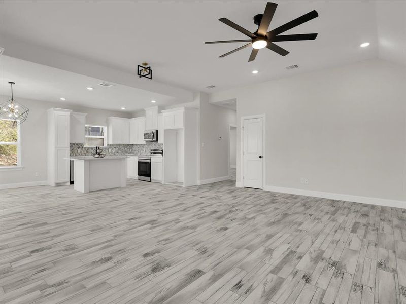 Unfurnished living room with lofted ceiling, light hardwood / wood-style flooring, and ceiling fan with notable chandelier