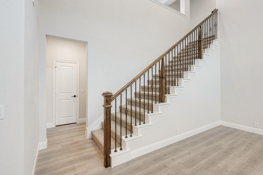 Carpeted staircase with wood handrail and iron balusters in an open entryway with light hardwood floors