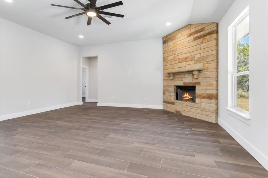 Unfurnished living room with vaulted ceiling, a stone fireplace, and ceiling fan