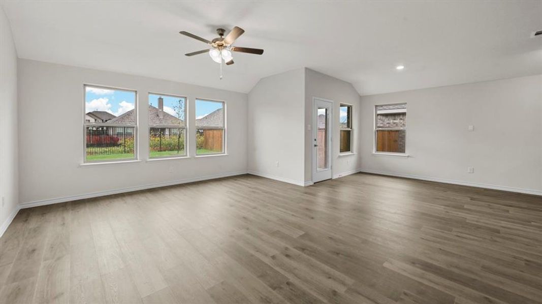 Spacious room featuring wood-finish flooring, light-colored walls, multiple windows, a ceiling fan with integrated lighting, and a glass-paneled exterior door