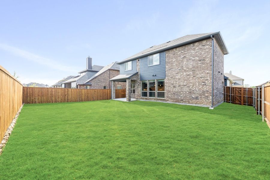 Backyard of two-story brick home with large green lawn and wood privacy fence