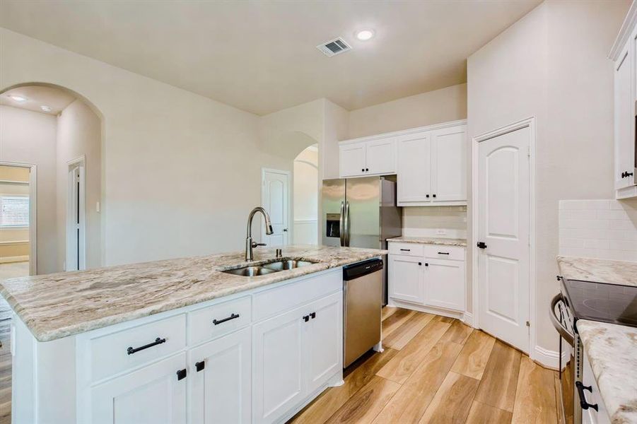 Kitchen featuring white cabinetry, light hardwood / wood-style floors, sink, a center island with sink, and stainless steel appliances