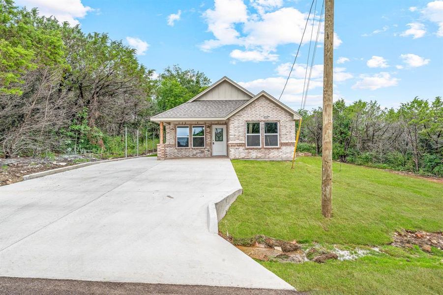 View of front facade featuring brick siding, concrete driveway, a front lawn, a shingled roof, and board and batten siding View of front facade featuring brick siding, concrete driveway, a front lawn, a shingled roof, and board and batten siding