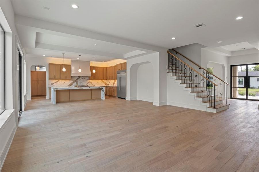 Unfurnished living room featuring a tray ceiling, stairway, light wood finished floors, and recessed lighting Unfurnished living room featuring a tray ceiling, stairway, light wood finished floors, and recessed lighting