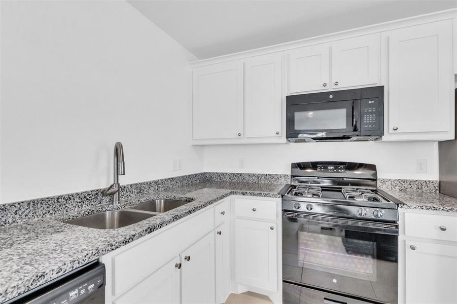 Kitchen featuring black appliances, white cabinetry, and light stone counters