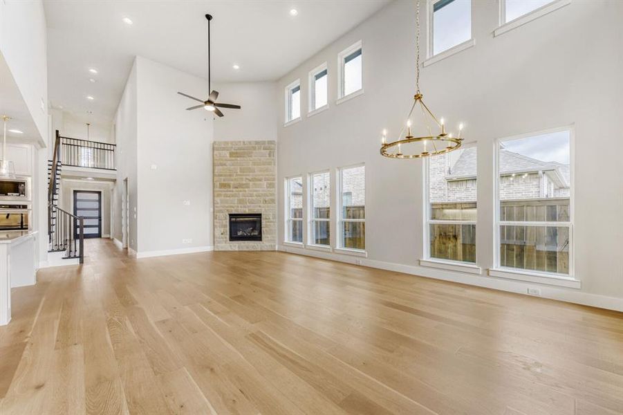 Unfurnished living room featuring a stone fireplace, ceiling fan, a high ceiling, hanging lights, and light wood-style flooring