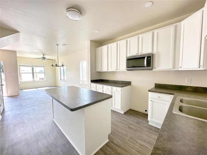 Kitchen featuring dark countertops, stainless steel microwave, a center island, white cabinetry, and open floor plan
