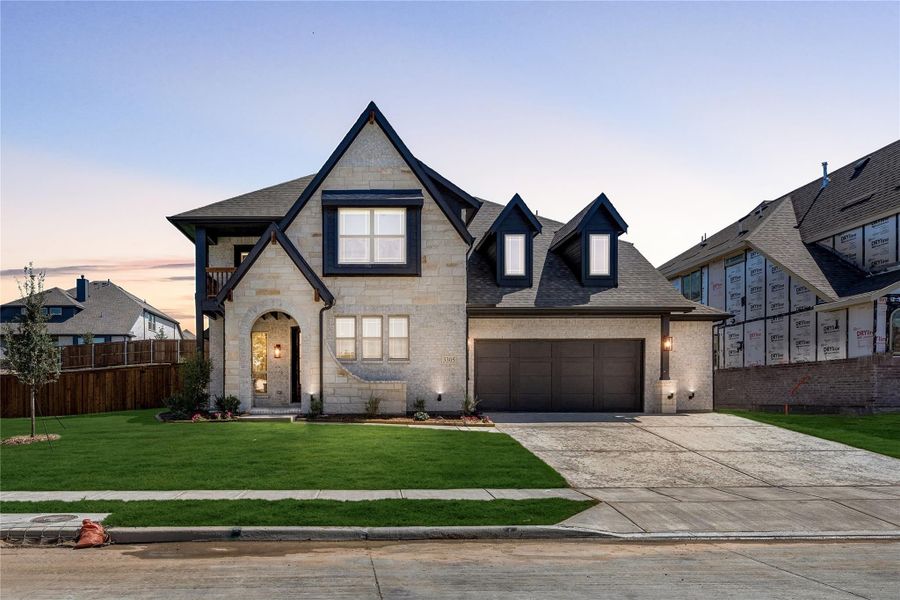 Two-story stone home with dark trim, arched entry, two-car garage, and manicured front lawn at dusk Two-story stone home with dark trim, arched entry, two-car garage, and manicured front lawn at dusk