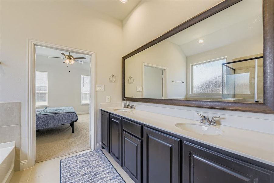Ensuite bathroom with double vanity, light tile patterned flooring, a bath, a shower stall, and a ceiling fan