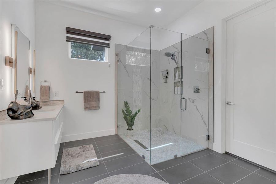 Bathroom with a marble finish shower, vanity, and dark tile patterned flooring