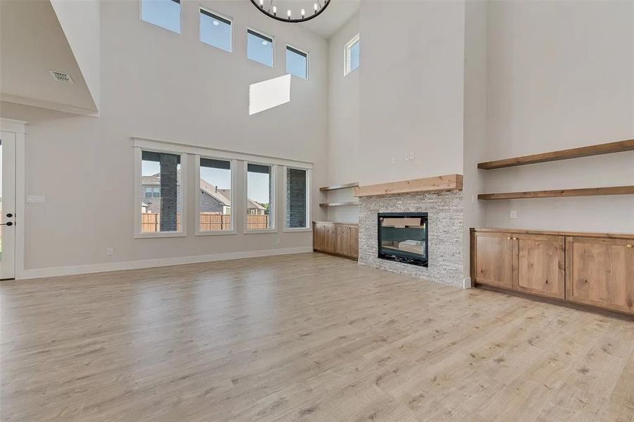 Unfurnished living room featuring light wood-type flooring, a glass covered fireplace, a high ceiling, and suspended lighting