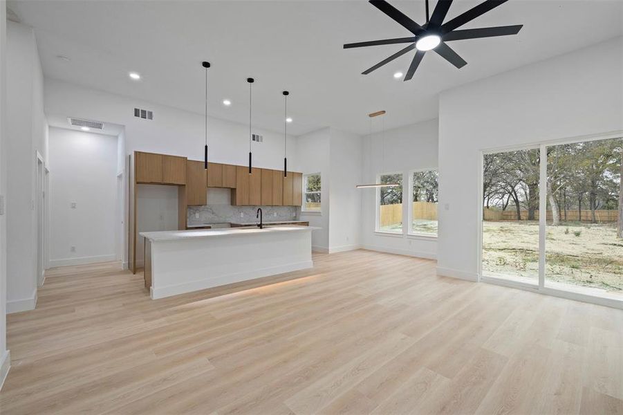 Kitchen featuring modern cabinets, a kitchen island with sink, brown cabinetry, tasteful backsplash, and light wood-style floors