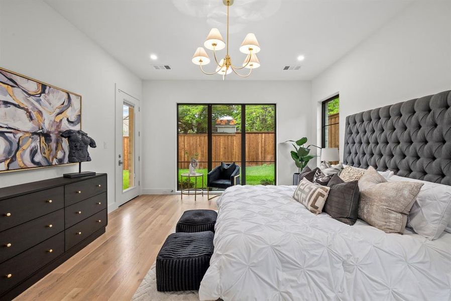 This bedroom features light wood flooring, large windows overlooking a fenced yard, and a door providing direct outdoor access