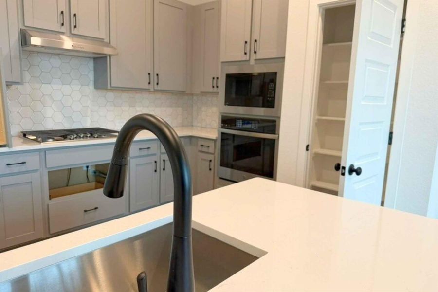 Kitchen with stainless steel appliances, tasteful backsplash, light stone countertops, and gray cabinets