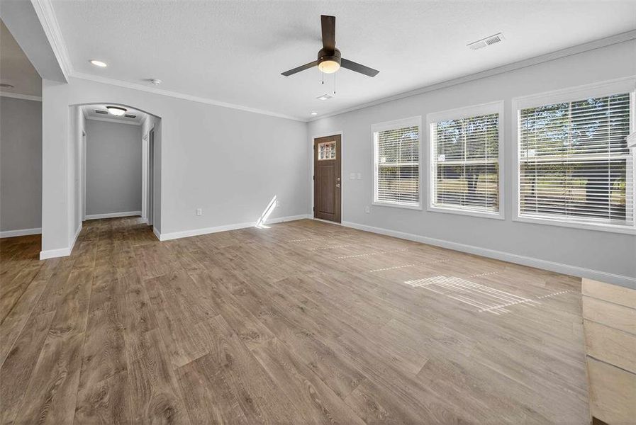 Unfurnished living room with crown molding, light wood finished floors, arched walkways, ceiling fan, and recessed lighting Unfurnished living room with crown molding, light wood finished floors, arched walkways, ceiling fan, and recessed lighting