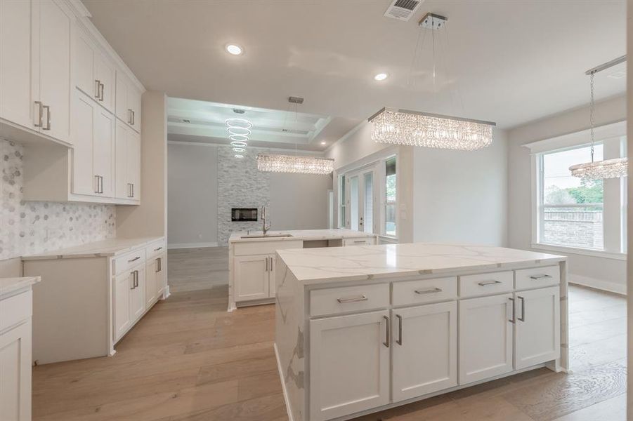 Kitchen featuring light wood finished floors, light stone countertops, white cabinets, hanging light fixtures, and a tray ceiling